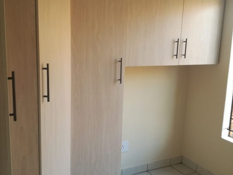 A clean, empty bedroom featuring light wood-finish built-in cupboards and neutral tiled flooring, offering a versatile space ready for personalization.