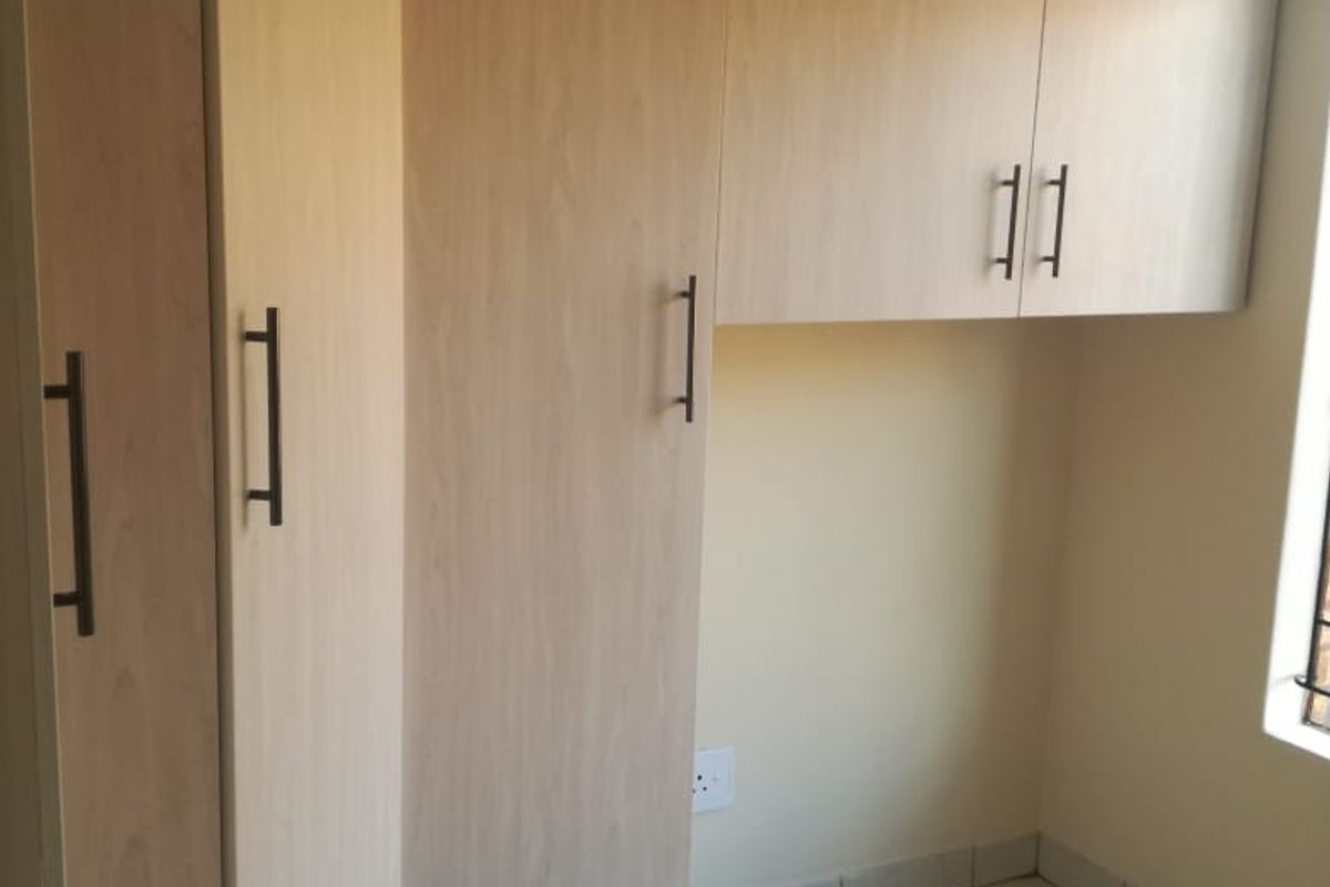 A clean, empty bedroom featuring light wood-finish built-in cupboards and neutral tiled flooring, offering a versatile space ready for personalization.