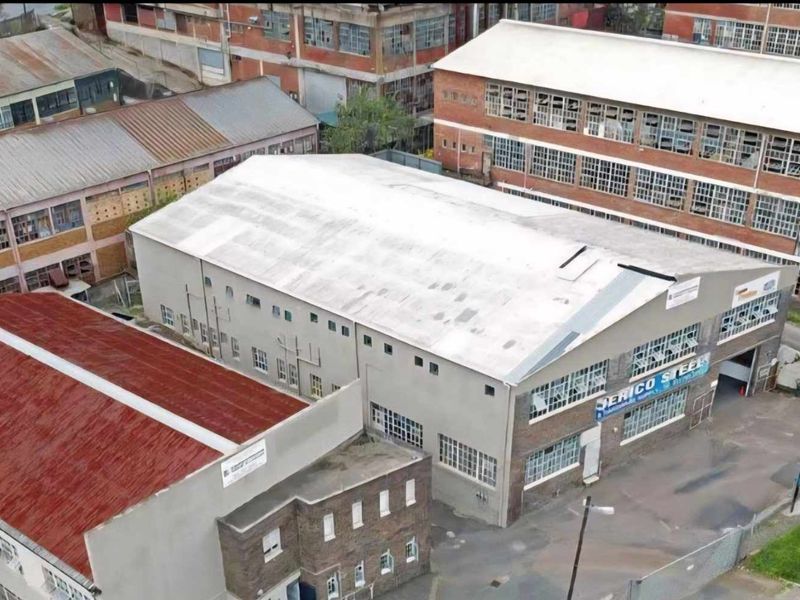 Aerial view of an industrial warehouse complex featuring multiple buildings with corrugated roofing and large multi-pane industrial windows.