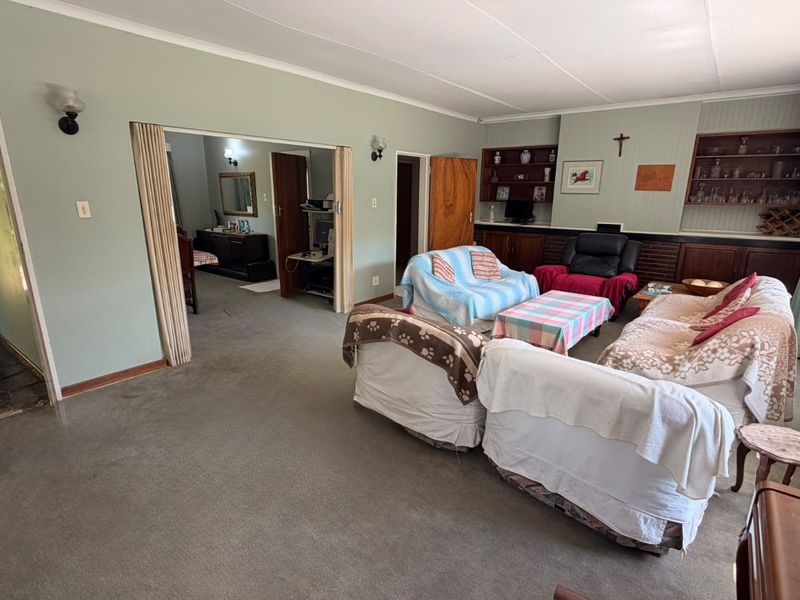 Spacious living room featuring built-in shelving, a brick fireplace surround, and carpet flooring, offering a comfortable layout with access to adjacent rooms.