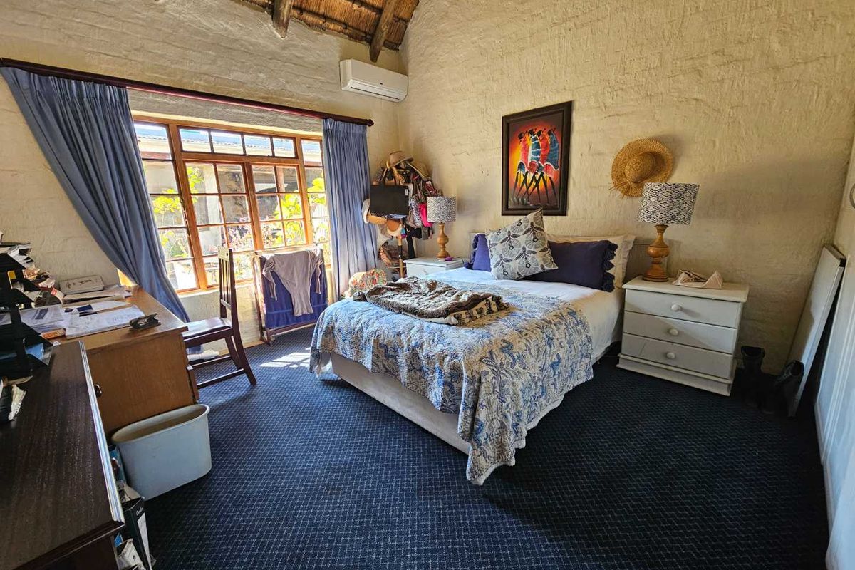 A rustic bedroom featuring a high thatched ceiling with exposed rafters, textured stone walls, and a split-system air conditioner.
