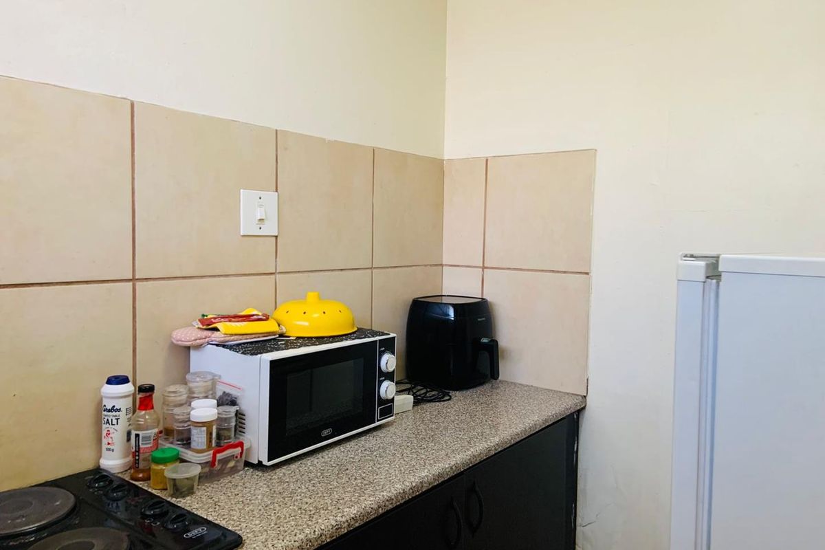 A compact kitchen area featuring a tiled backsplash, laminate countertop, and built-in cabinetry with an integrated electric hob.