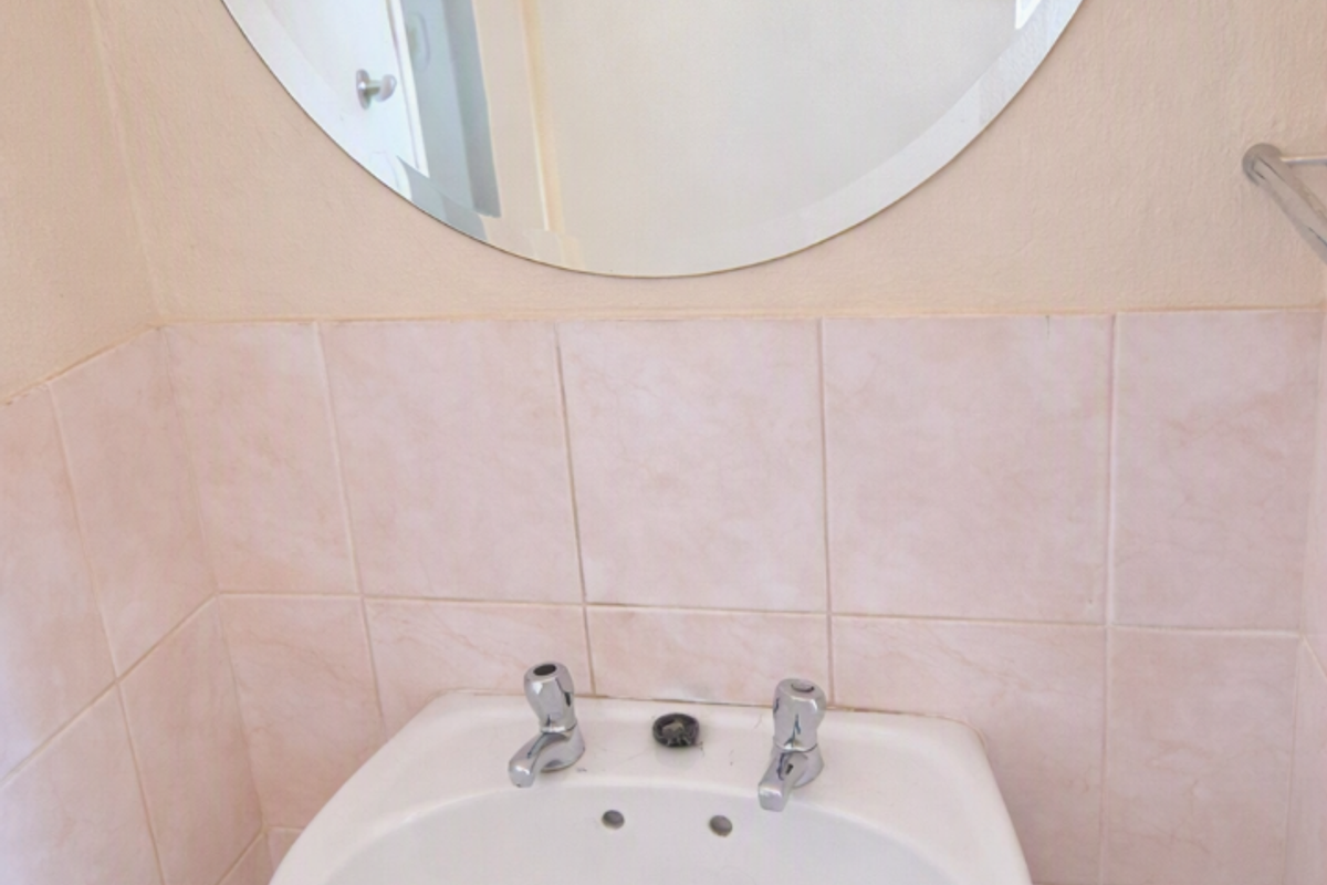 A compact bathroom featuring a white pedestal basin, wall-mounted mirror, and neutral ceramic wall tiling.