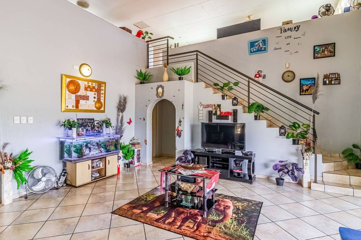 Spacious open-plan living area featuring tiled flooring, a prominent staircase with metal balustrade, and an architectural archway leading to adjacent rooms.