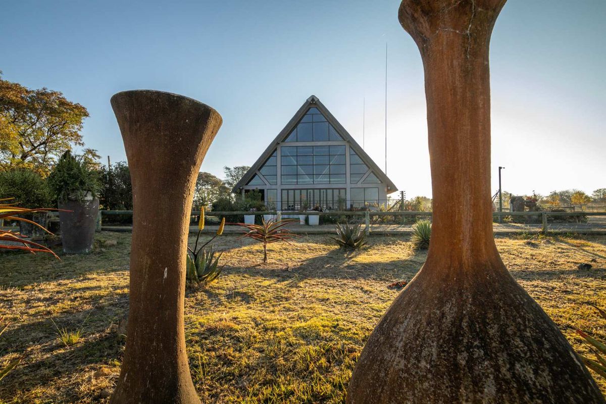 A scenic view of the rear of a unique A-frame guest house structure, featuring a large glass facade set within a landscaped garden.