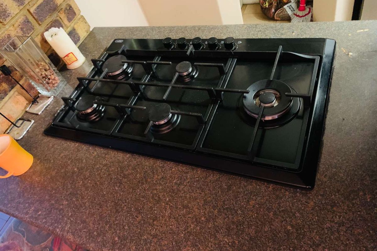 A close-up view of a built-in black gas hob set into a dark granite countertop with a brick feature wall in the background.