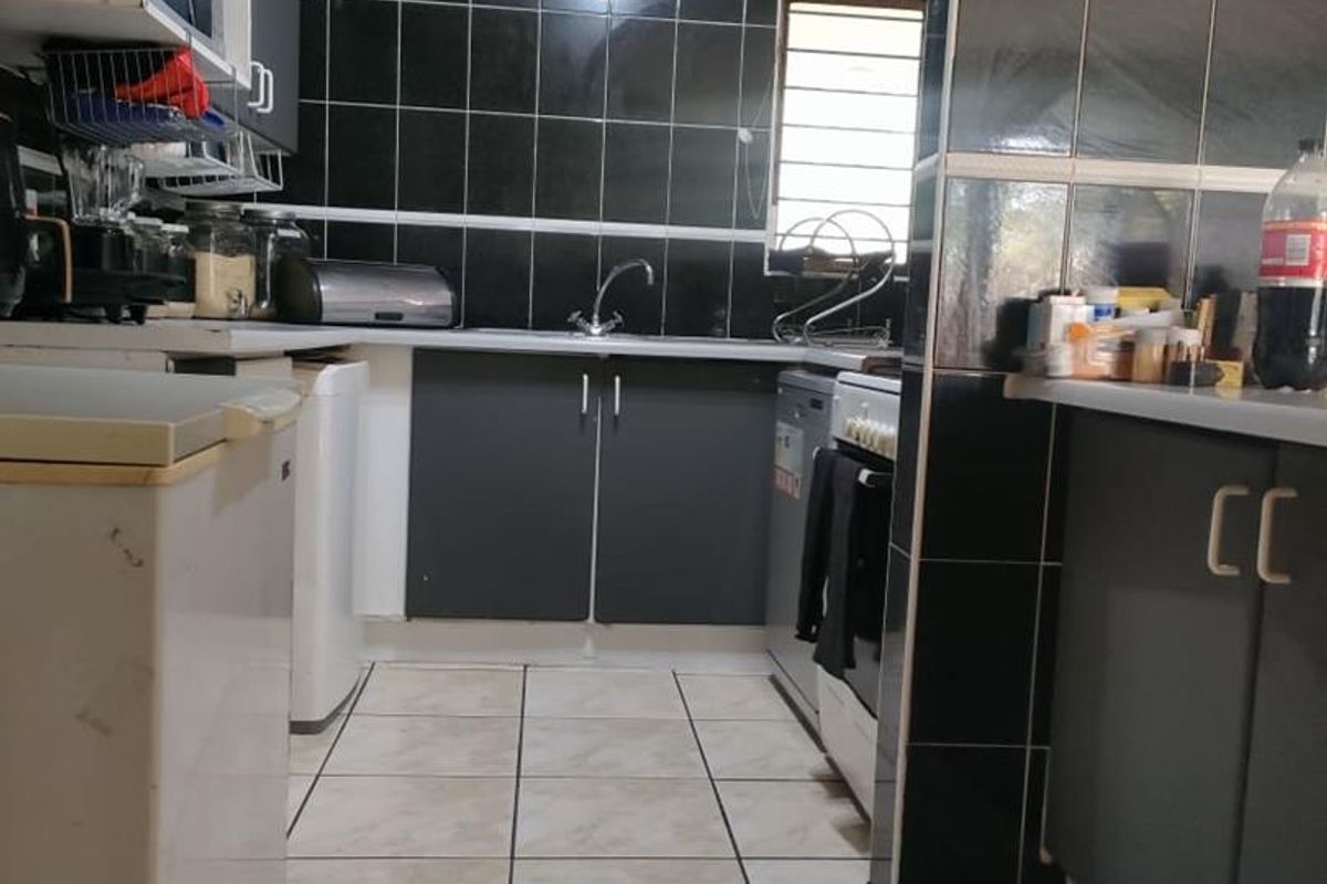 A functional kitchen featuring dark cabinetry, a black tiled backsplash, tiled flooring, and a stainless steel sink with a freestanding stove.