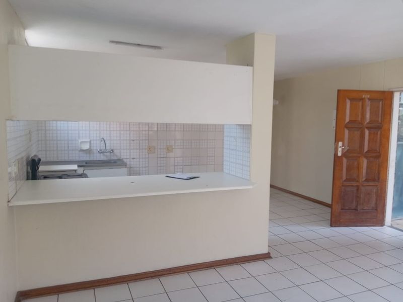 An open-plan living area featuring a kitchen pass-through, tiled flooring, and a wooden entrance door in a vacant apartment setting.