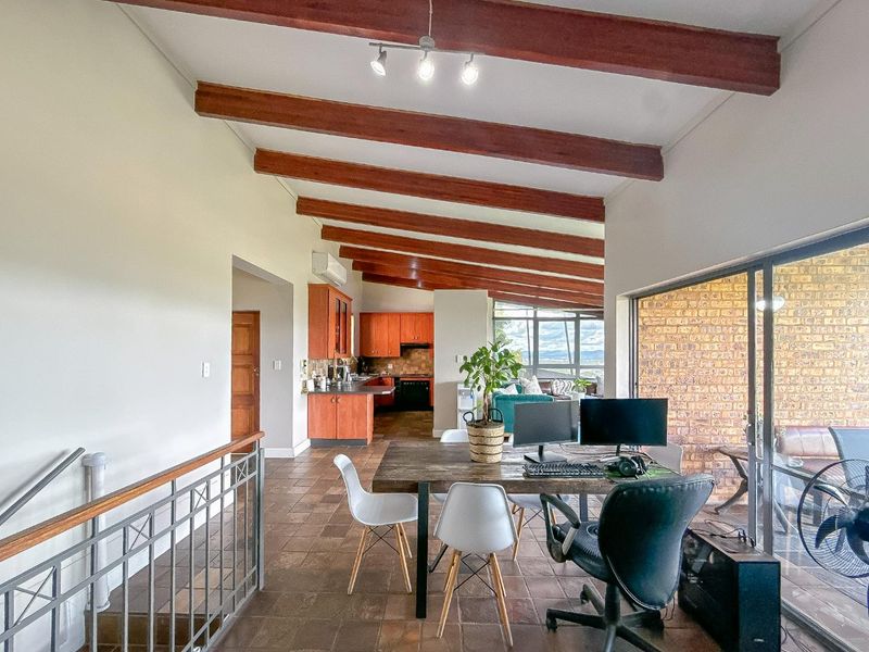 Spacious open-plan living area featuring exposed timber beams, tiled flooring, an exposed brick feature wall, and a functional kitchen with built-in cabinetry.
