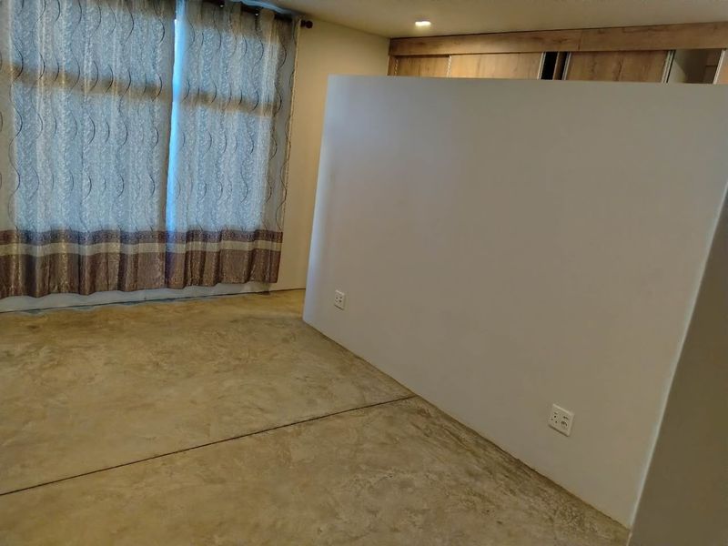 An empty bedroom featuring polished concrete flooring, built-in cupboards, and a partition wall, offering a blank canvas for custom interior design.
