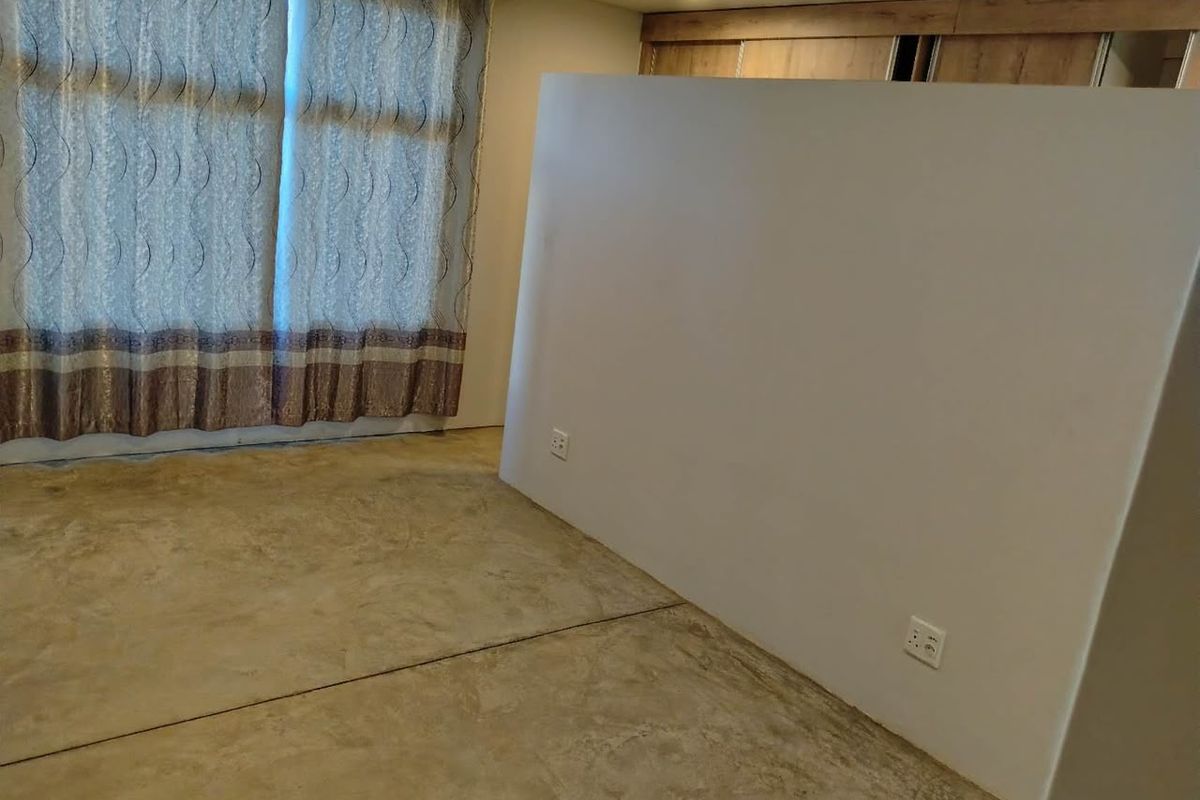 An empty bedroom featuring polished concrete flooring, built-in cupboards, and a partition wall, offering a blank canvas for custom interior design.