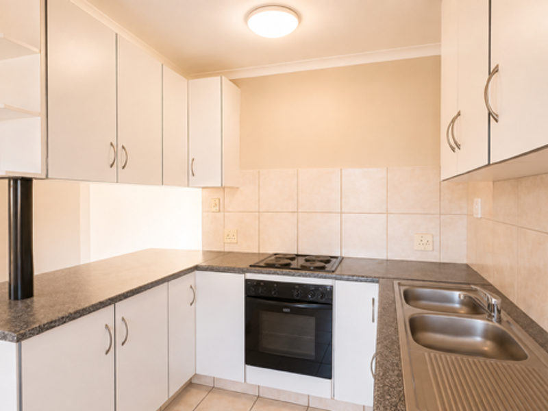 A functional kitchen featuring white cabinetry, laminate countertops, a built-in oven with electric hob, and a double stainless steel sink with tiled splashback.