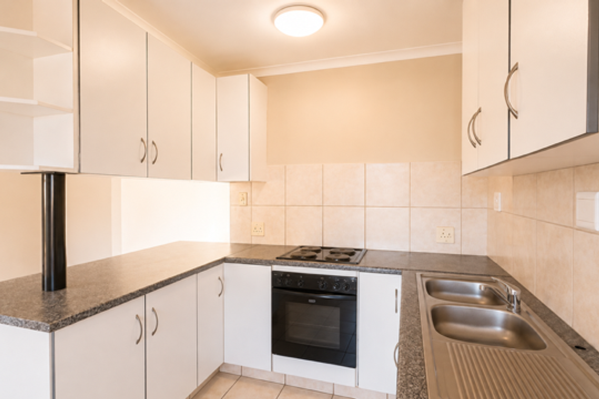 A functional kitchen featuring white cabinetry, laminate countertops, a built-in oven with electric hob, and a double stainless steel sink with tiled splashback.