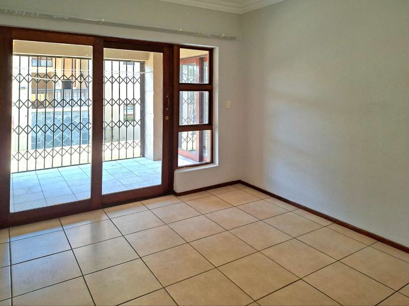 An empty living room featuring neutral tiled flooring, wooden sliding doors with security gates, and access to an outdoor patio area.