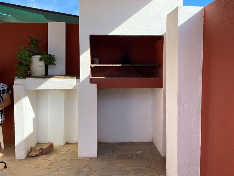 Outdoor patio area featuring a built-in braai, stone flooring, and a covered roof structure, ideal for entertaining.