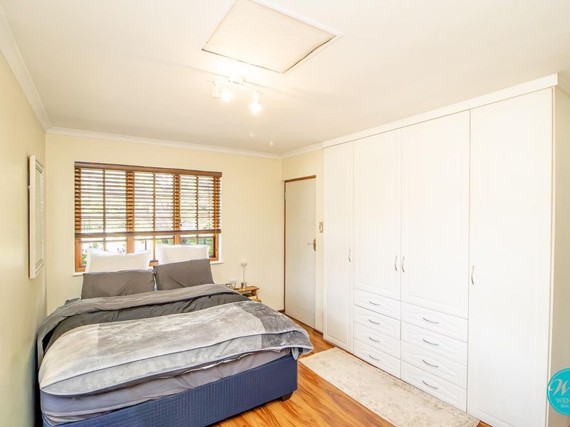 A well-maintained bedroom featuring polished timber flooring, extensive built-in cabinetry, and natural light filtered through venetian blinds.