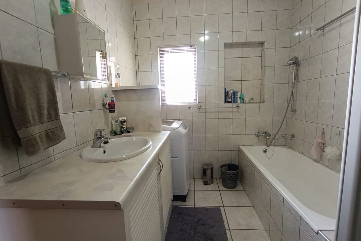 A functional bathroom featuring a built-in vanity with basin, a bathtub with shower mixer, and tiled walls and flooring.