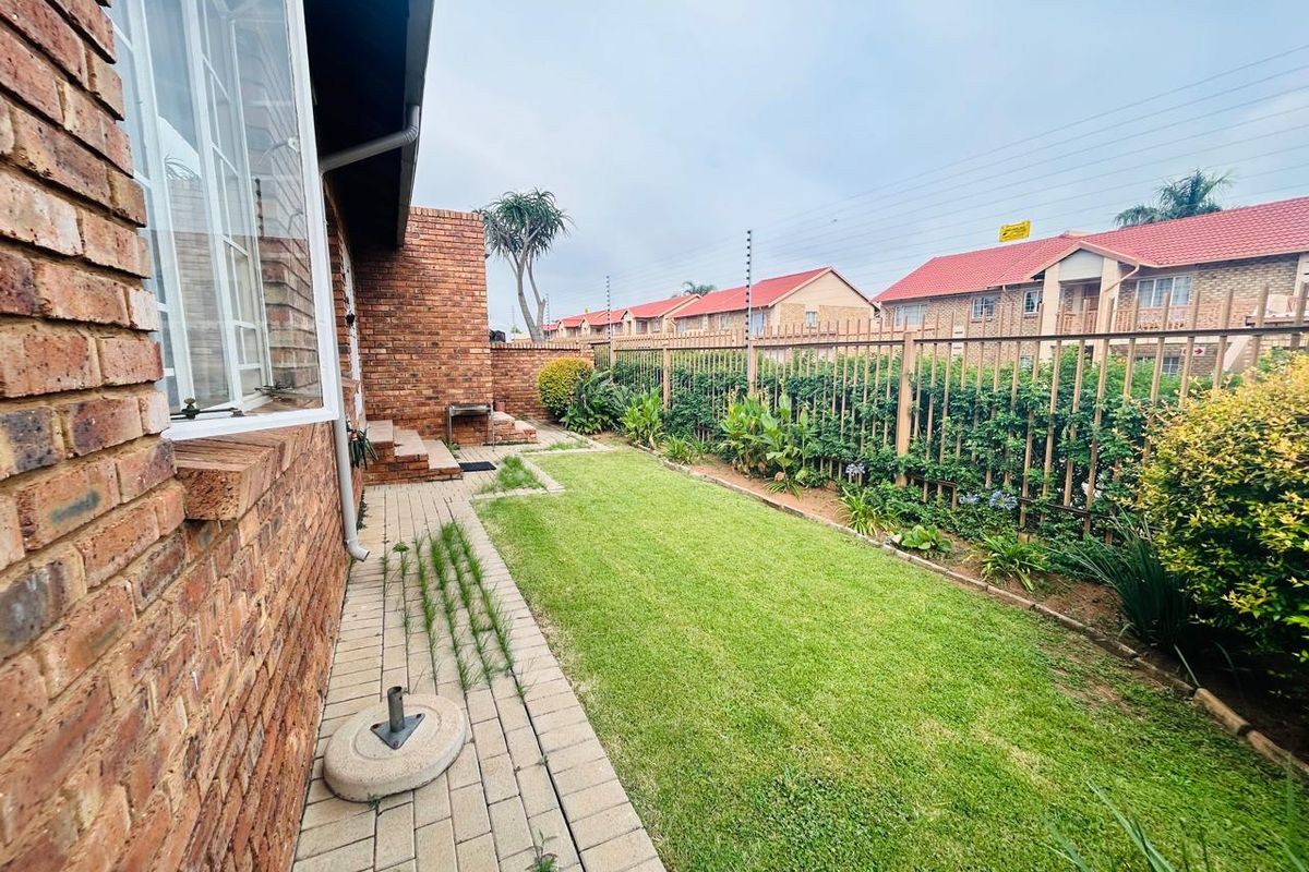 A private rear garden featuring a brick-paved walkway, a well-maintained lawn, and secure perimeter fencing with integrated electric security wires.