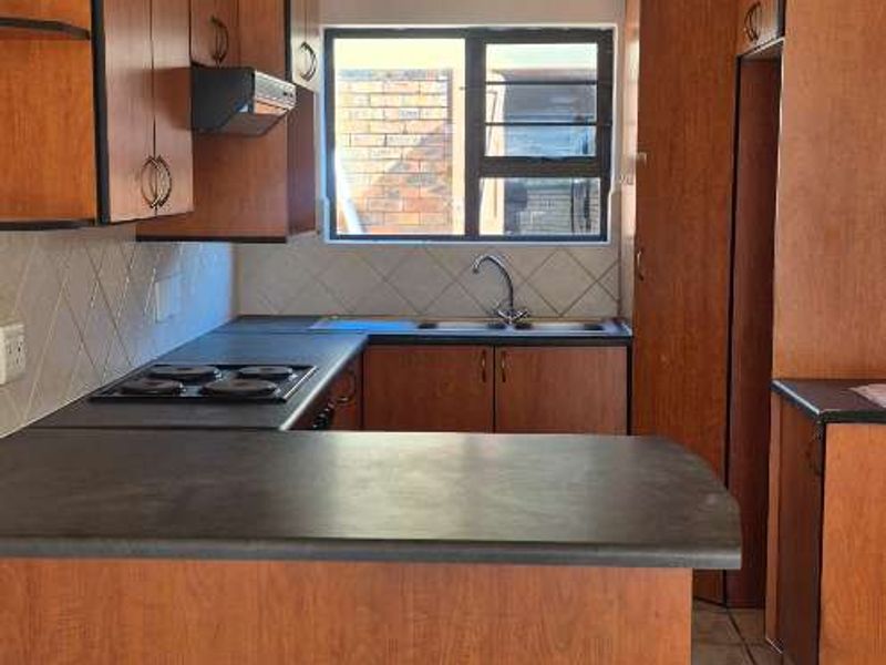 A functional kitchen featuring wooden cabinetry, laminate countertops, an electric hob, and tiled flooring, offering a clean and practical workspace.