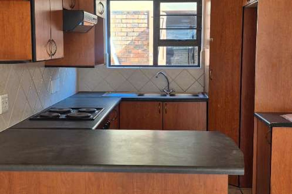 A functional kitchen featuring wooden cabinetry, laminate countertops, an electric hob, and tiled flooring, offering a clean and practical workspace.