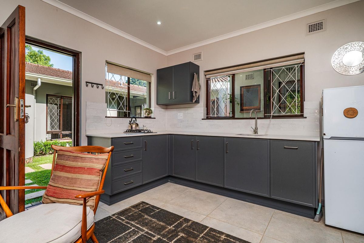 Modern kitchen featuring dark grey cabinetry, white subway tile backsplash, stone countertops, and a stainless steel sink with direct access to the garden.