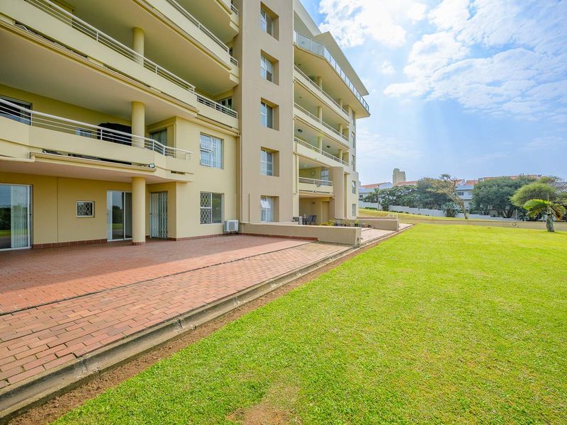 Rear view of the townhouse complex featuring a spacious paved patio area, multiple balconies, and a well-maintained communal lawn.