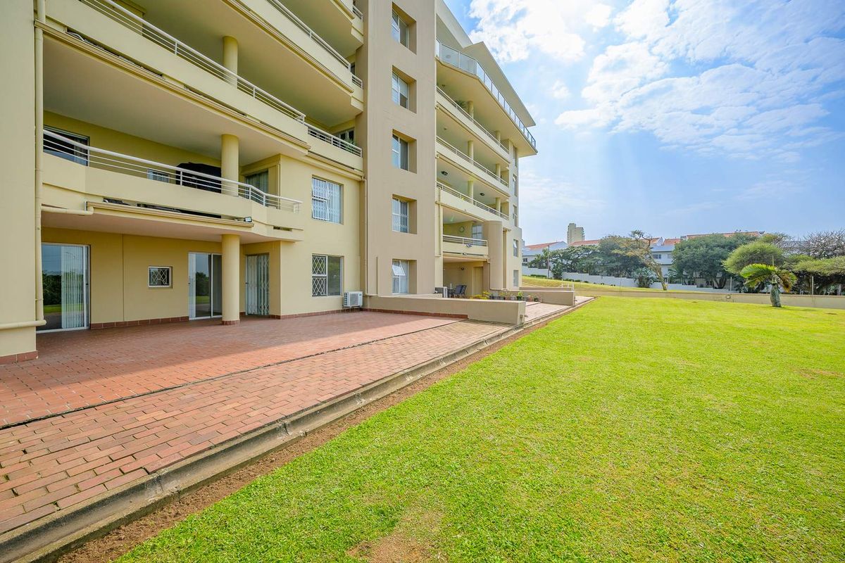 Rear view of the townhouse complex featuring a spacious paved patio area, multiple balconies, and a well-maintained communal lawn.