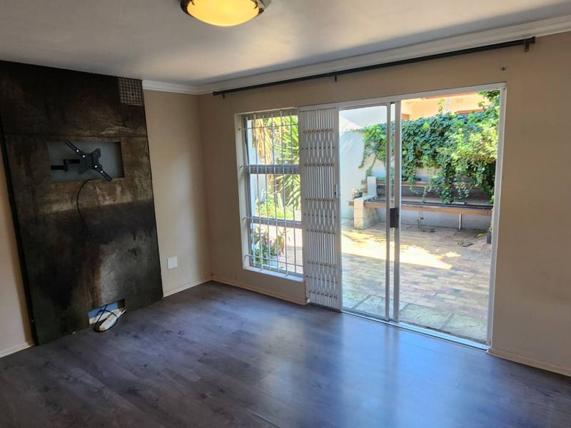 An empty living room featuring laminate flooring, a built-in feature wall, and sliding glass doors providing access to a private patio area.