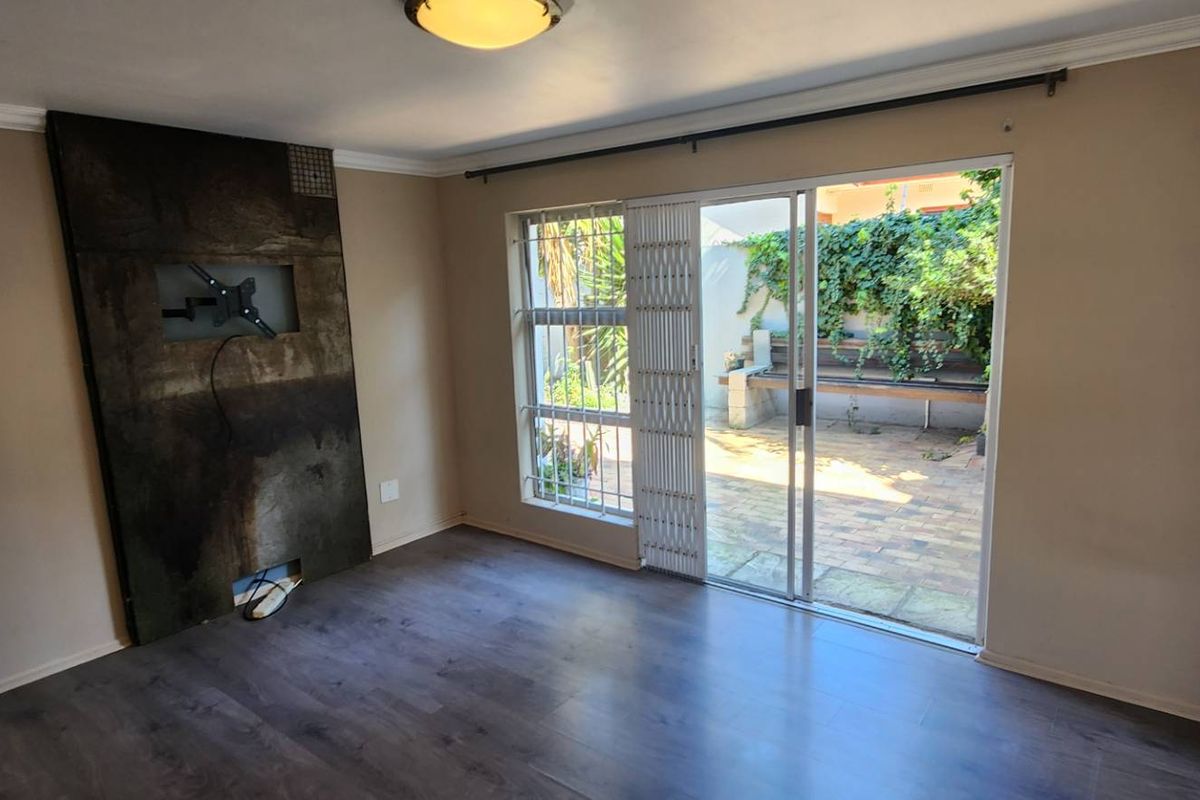 An empty living room featuring laminate flooring, a built-in feature wall, and sliding glass doors providing access to a private patio area.
