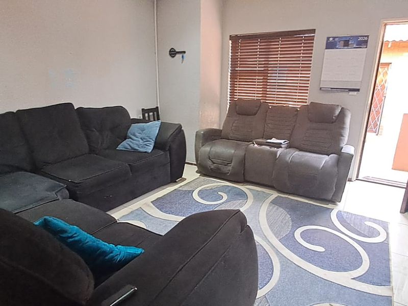 A functional living room featuring tiled flooring, venetian blinds, and direct access to an outdoor area through a security gate.