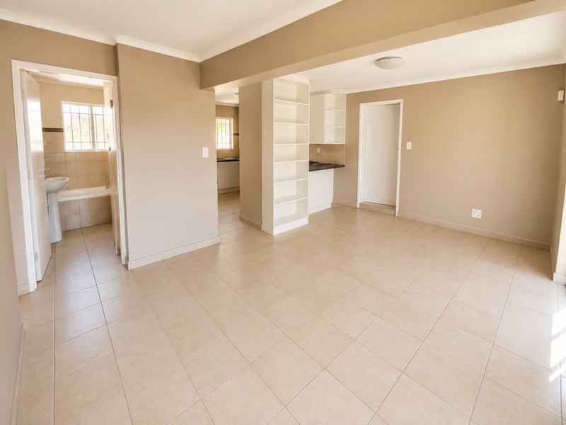 Spacious open-plan living area featuring neutral tiled flooring, built-in shelving, and direct access to an adjacent bathroom and kitchen area.