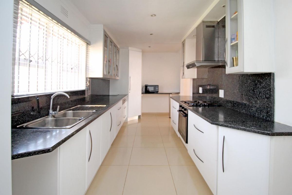 Modern galley-style kitchen featuring white cabinetry, dark granite countertops, stainless steel oven, gas hob, extractor fan, and double basin sink.