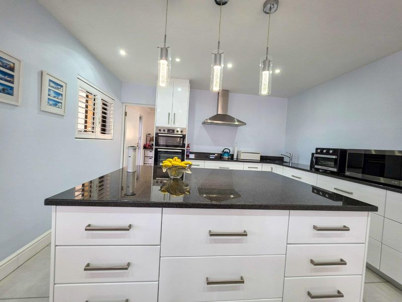 Modern kitchen featuring a large central island with granite countertops, white cabinetry, built-in oven, and contemporary pendant lighting.