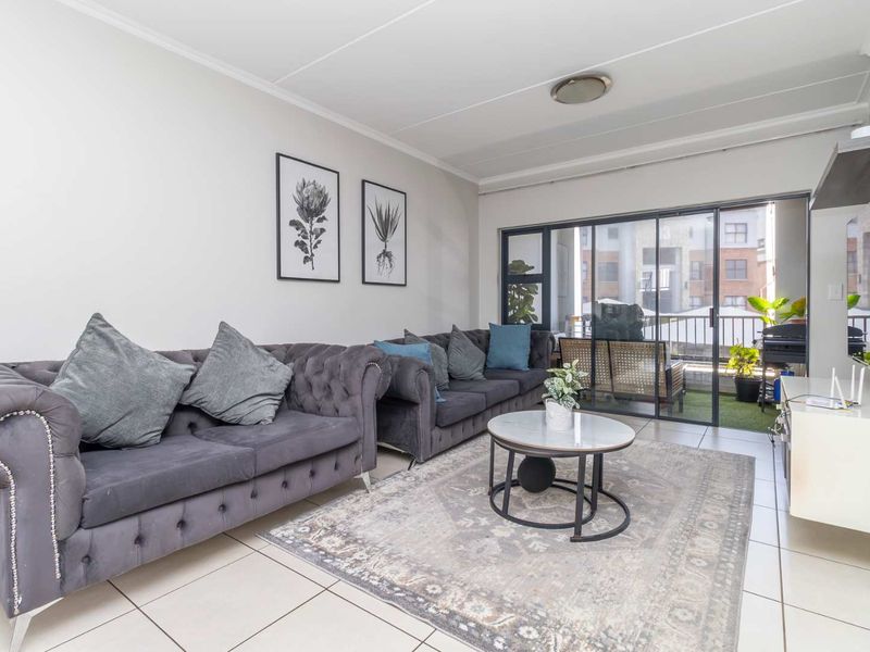A bright living room featuring tiled flooring and large sliding glass doors that provide access to an adjoining balcony.