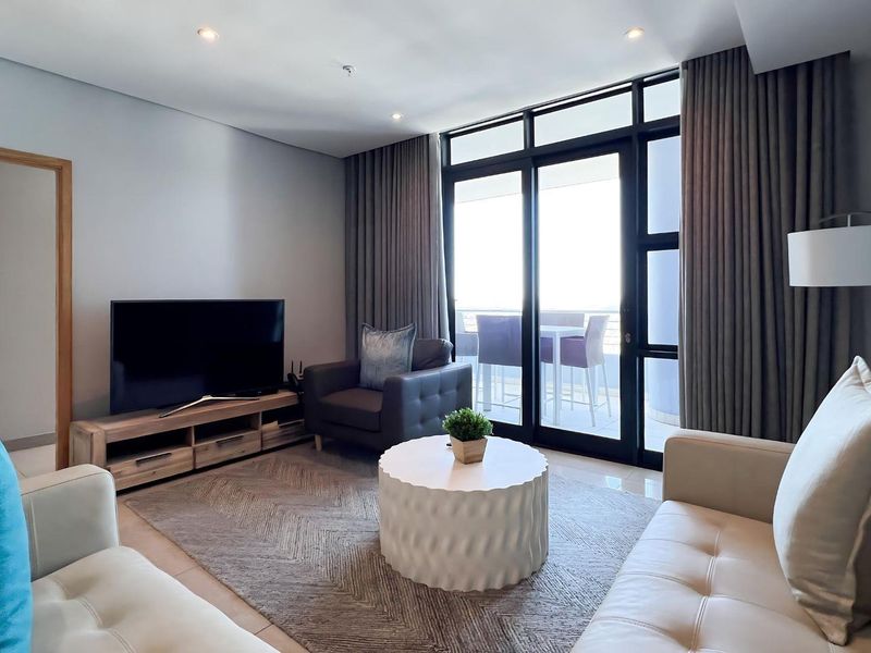 A well-maintained living room featuring tiled flooring, recessed lighting, and large sliding glass doors providing access to an outdoor balcony area.