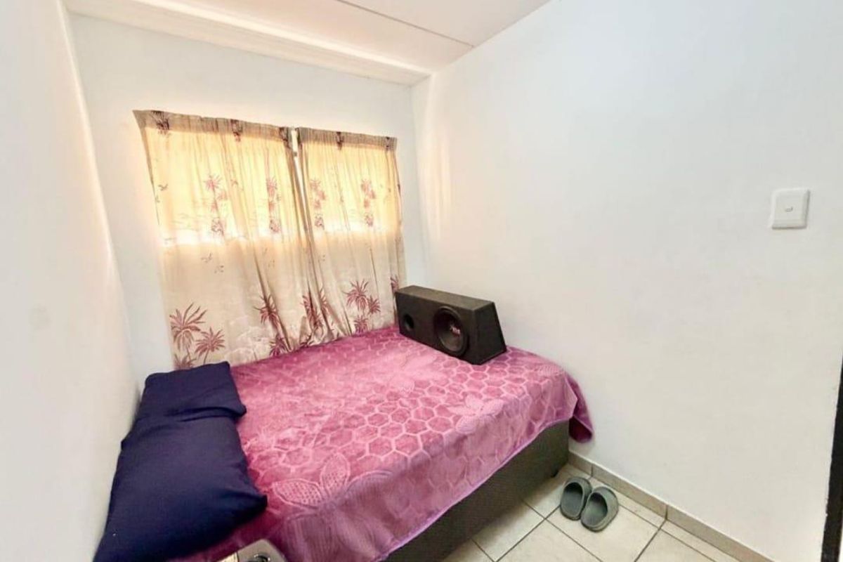 A compact bedroom featuring tiled flooring and a window with curtains, providing a functional space for rest.