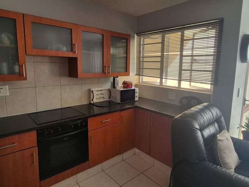 Compact kitchen featuring wooden cabinetry, granite countertops, built-in oven and hob, and tiled flooring with natural light from the adjacent window.