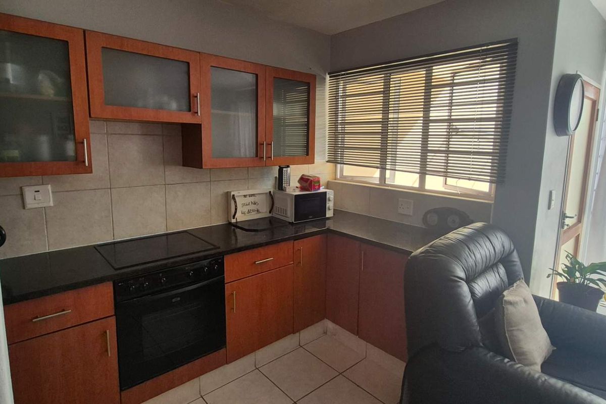 Compact kitchen featuring wooden cabinetry, granite countertops, built-in oven and hob, and tiled flooring with natural light from the adjacent window.