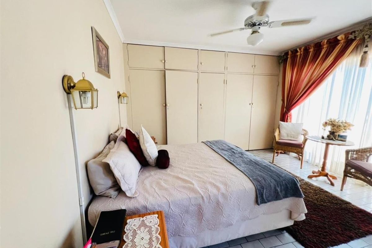 A bedroom featuring built-in floor-to-ceiling cupboards, a ceiling fan, and tiled flooring with access to natural light.