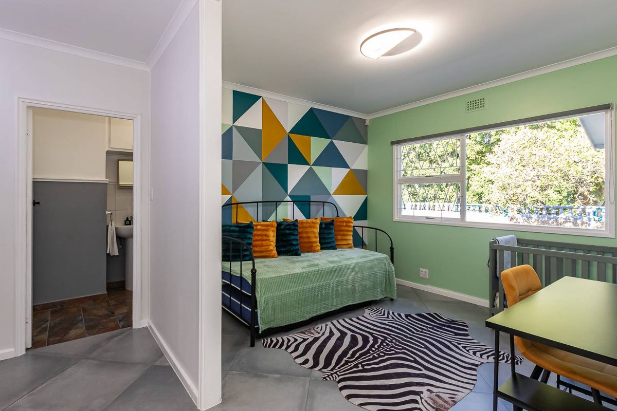 A bright bedroom featuring tiled flooring, a geometric accent wall, and a window with security bars, with an adjacent bathroom visible.