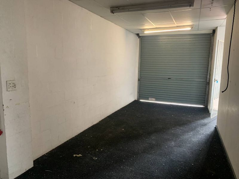 An empty, utilitarian garage space featuring a roller shutter door, suspended ceiling, and exposed blockwork walls, suitable for storage or workshop use.