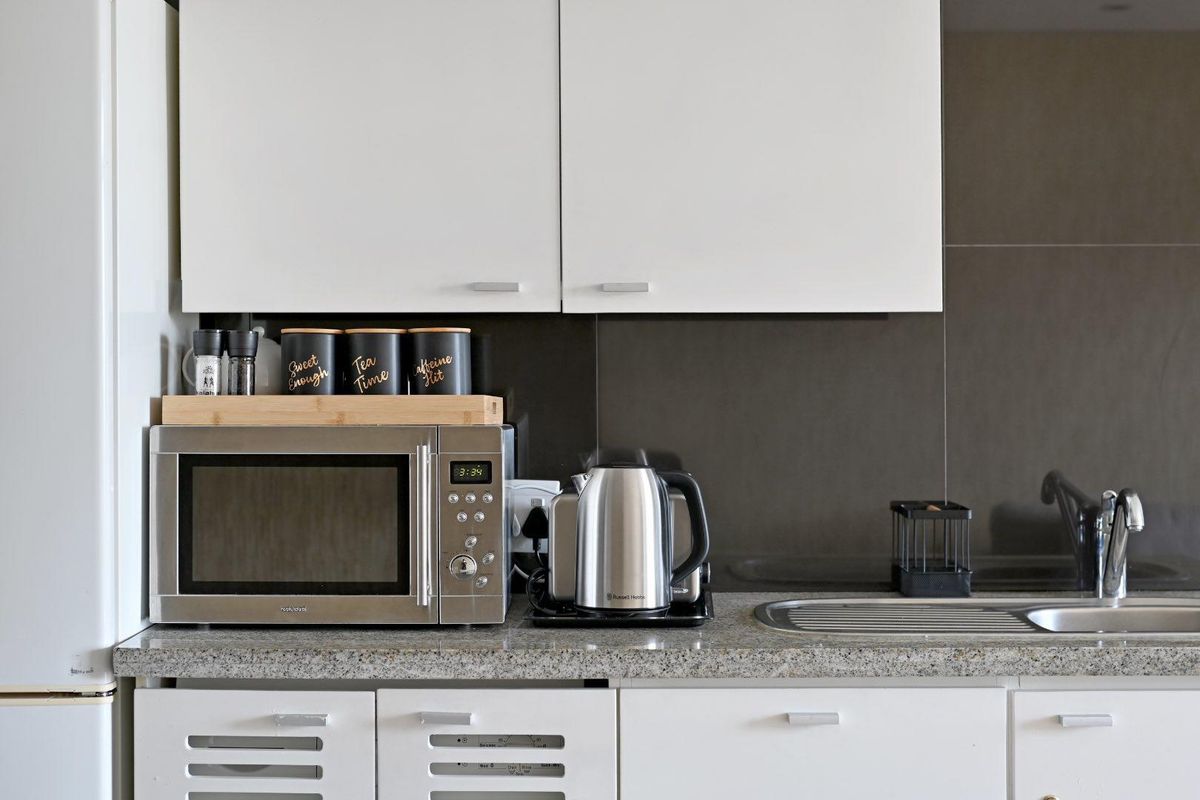 A clean kitchen area featuring white cabinetry, granite countertops, a stainless steel sink, and a dark tiled splashback.