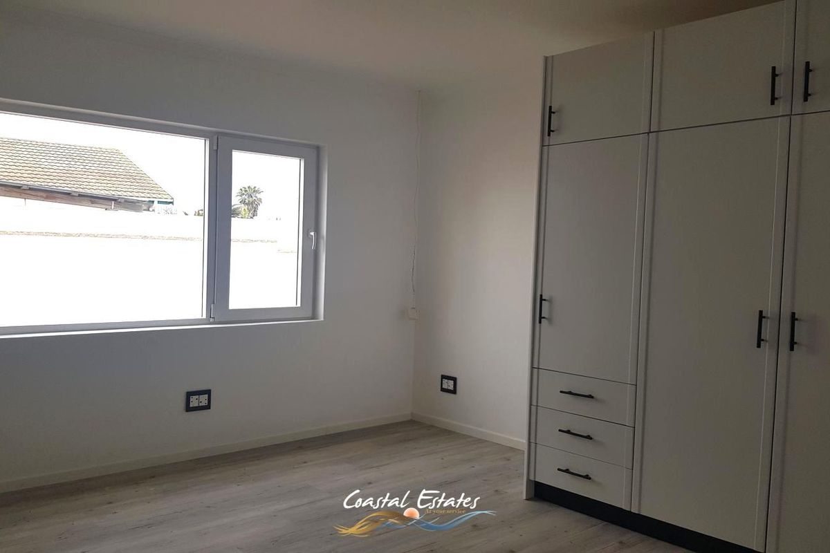 A bright, empty bedroom featuring modern laminate flooring, white walls, and a large built-in wardrobe with contemporary hardware.