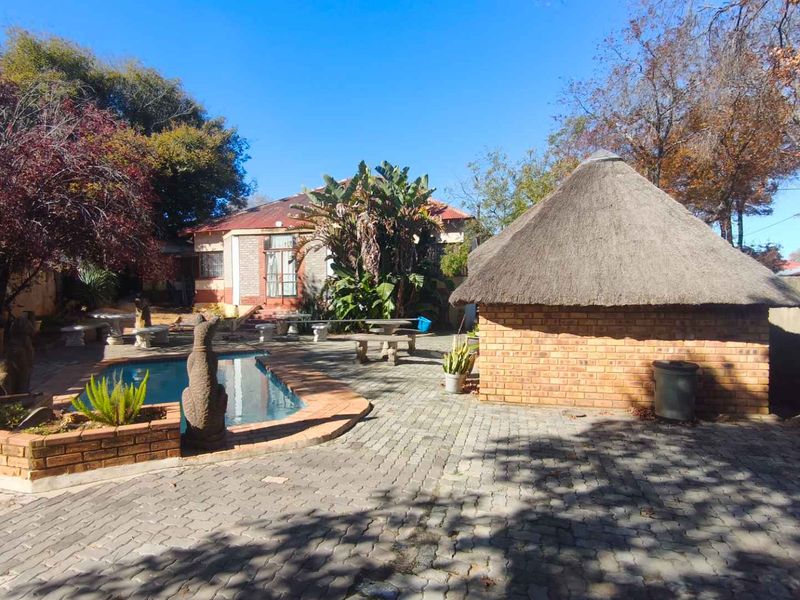 Rear garden area featuring a swimming pool, paved patio space, and a traditional thatch lapa structure.