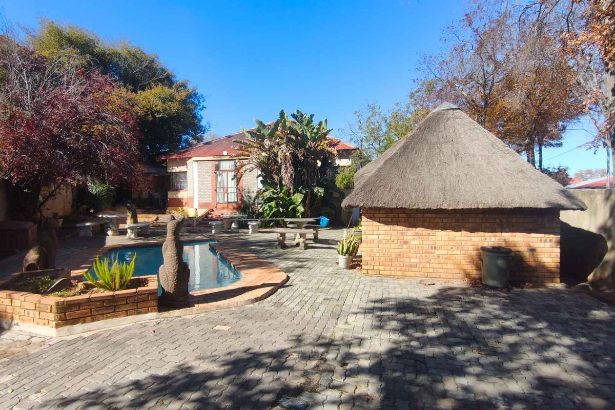 Rear garden area featuring a swimming pool, paved patio space, and a traditional thatch lapa structure.