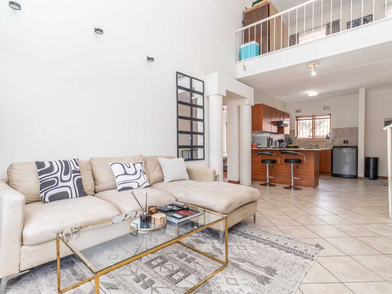 Open-plan living area featuring tiled floors, a mezzanine level with a metal balustrade, and an integrated kitchen with wooden cabinetry.