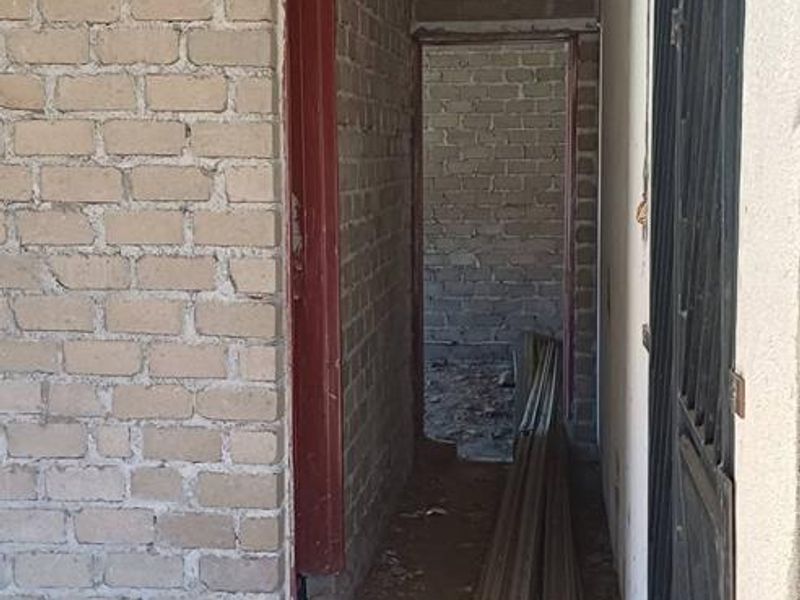 An unfinished utility space or corridor under construction featuring exposed brick walls, metal roof trusses, and a security gate.