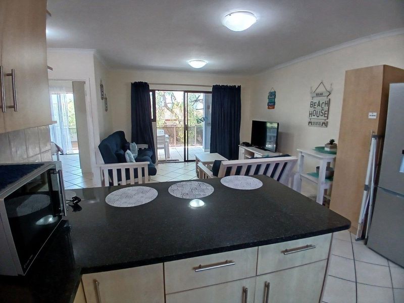 Open-plan living area featuring a kitchen with granite countertops, tiled flooring, and direct access to a private balcony through sliding glass doors.