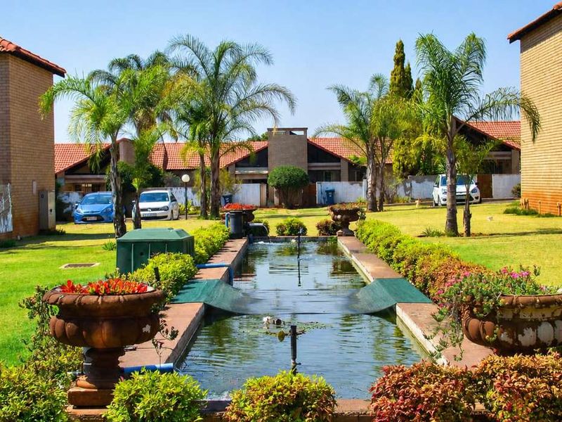 A communal garden area featuring a central water feature, brick-paved pathways, and established palm trees between townhouse units.