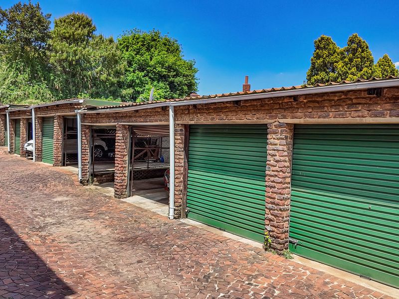 A row of secure garage units featuring exposed brick pillars, green roller shutter doors, and a durable cobblestone driveway.
